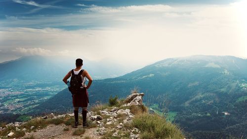 Rear view of man standing on mountain against sky