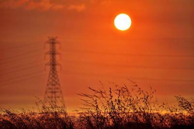 Silhouette electricity pylon on field against orange sky