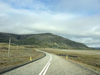 Empty road leading towards mountains against sky