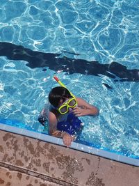 High angle view of boy with snorkel goggles and tube in swimming pool