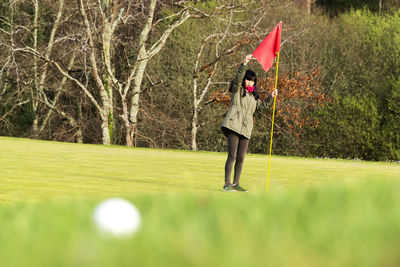 Full length of girl holding flag on golf course against trees