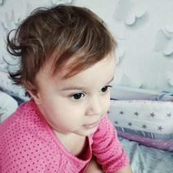 Close-up of thoughtful baby girl sitting on bed