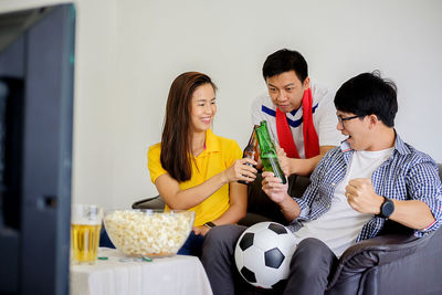 Friends toasting beer bottle while watching sport at home