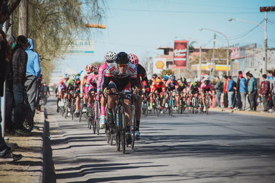 Cyclists riding bicycles on road against clear sky in city