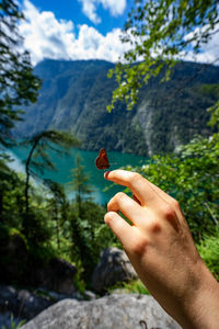 Midsection of person holding butterfly against mountain