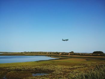 Airplane flying over landscape against clear blue sky