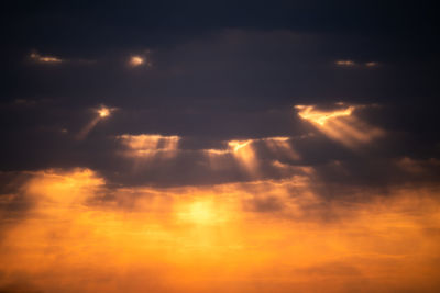 Low angle view of sunlight streaming through clouds during sunset