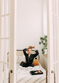 A happy pretty young woman in pajamas is resting and having breakfast in bed in a cozy apartment