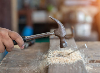 Close up of the carpenter hammering a nail into wooden stick in workshop.
