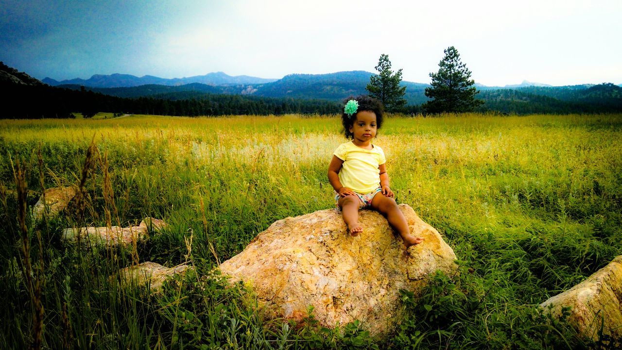 grass, casual clothing, lifestyles, field, full length, leisure activity, person, landscape, young adult, standing, grassy, looking at camera, sky, mountain, tranquility, nature, portrait, tranquil scene