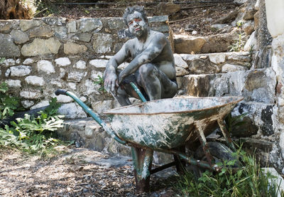 Portrait of man with facial mask sitting on rock by wheelbarrow