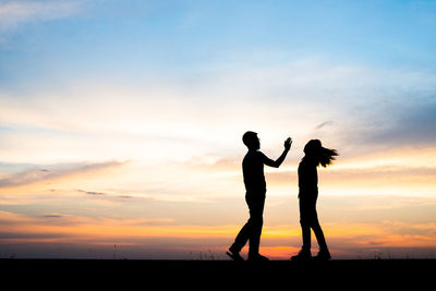 Silhouette man slapping woman against sky during sunset