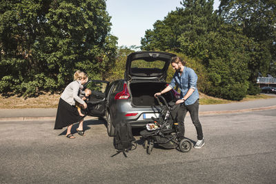 Mid adult parents with son and baby stroller near car on street