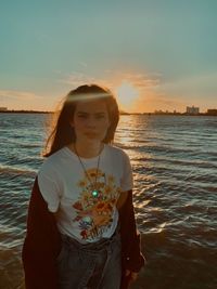 Portrait of young woman standing in sea against sky during sunset. 