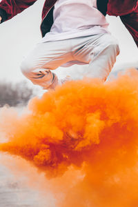 Low angle view of man jumping above orange smoke