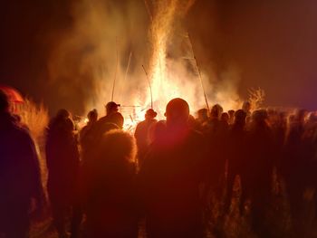 Rear view of people standing by bonfire at night
