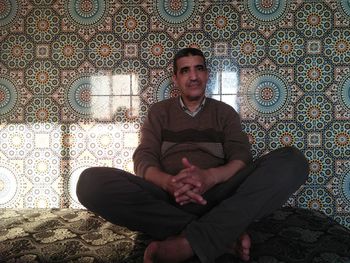 Mature man looking away while sitting against wall