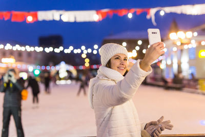 Young woman using mobile phone while standing on street in city at night