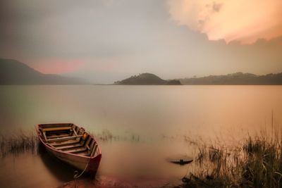 Boat moored in lake against sky during sunset