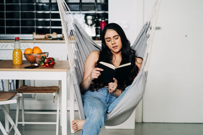 Young woman reading book while sitting on hammock