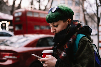 Portrait of non-binary hipster using smart phone standing in city