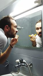 Man shaving while standing in front of mirror at bathroom