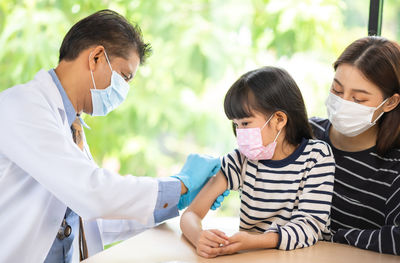 Doctor vaccinating girl sitting with mother