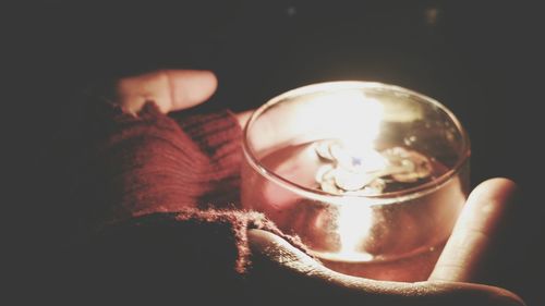 Cropped hands wearing fingerless gloves while holding illuminated tea light in darkroom