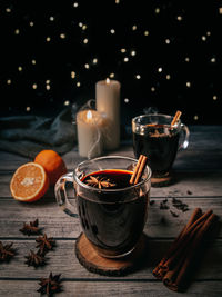 Still life of mugs filled with mulled wine at night on wooden table with spices and candles
