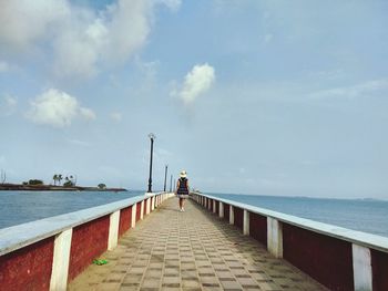 Rear view of woman walking on pier over sea against sky