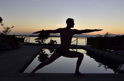 Full length of silhouette man practicing warrior position by pool against lake
