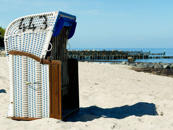 Hooded beach chair on shore against blue sky
