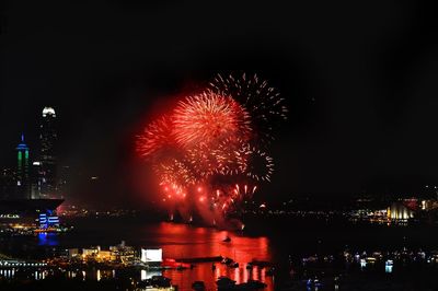 Firework display over illuminated city against sky at night