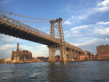 Low angle view of williamsburg bridge over east river against blue sky