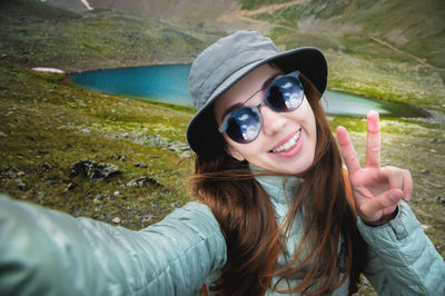 Young happy smiling tourist woman with long brunette hair and gray panama takes selfie with