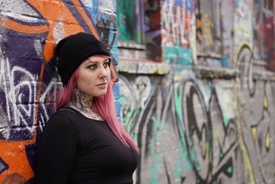 Young woman with pink hair standing against graffiti wall