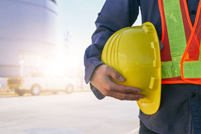 Midsection of man holding hardhat while standing outdoors