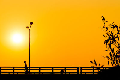 Silhouette person by street against orange sky