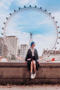 Man sitting on chain swing ride in city against sky