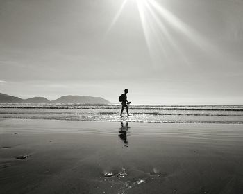 Silhouette person on shore at beach against sky