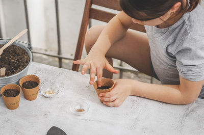 A little caucasian girl planting seeds in a cardboard cup with soil, pushing them with her finger