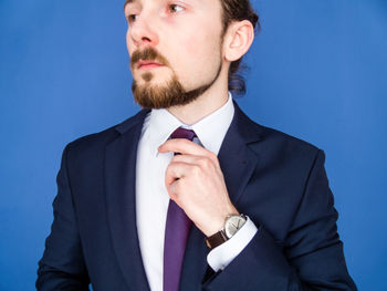 Young businessman adjusting tie against blue background