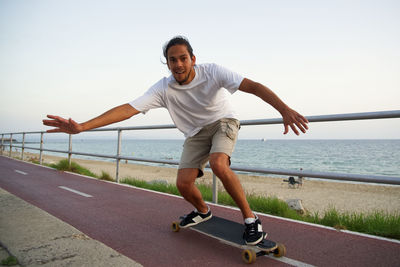 Portrait of man skateboarding on footpath against sea at sunset