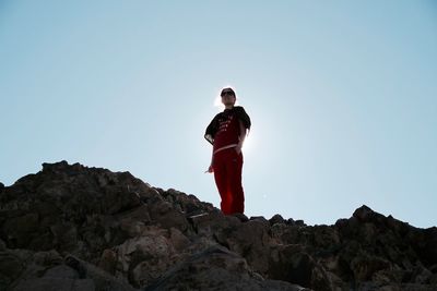 Low angle view of woman standing on rocks against clear sky