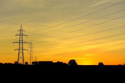 Low angle view of silhouette electricity pylon against sky during sunset