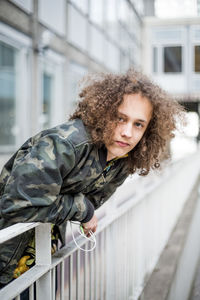 Portrait of confident teenage boy leaning on railing in city