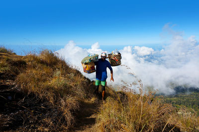 Man carrying baskets on mountain against sky