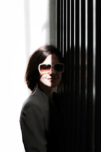 Portrait of woman wearing sunglasses standing against wall