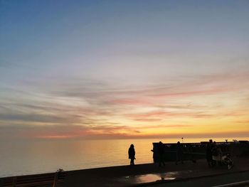 Silhouette people standing by sea against sky during sunset