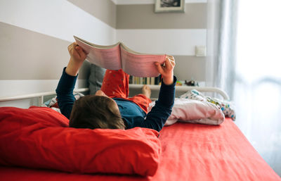 Rear view of siblings relaxing on bed at home